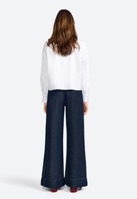White, long-sleeved blouse with elastic cuffs paired with wide-leg, dark blue denim jeans featuring a hem cuff detail and back pockets.