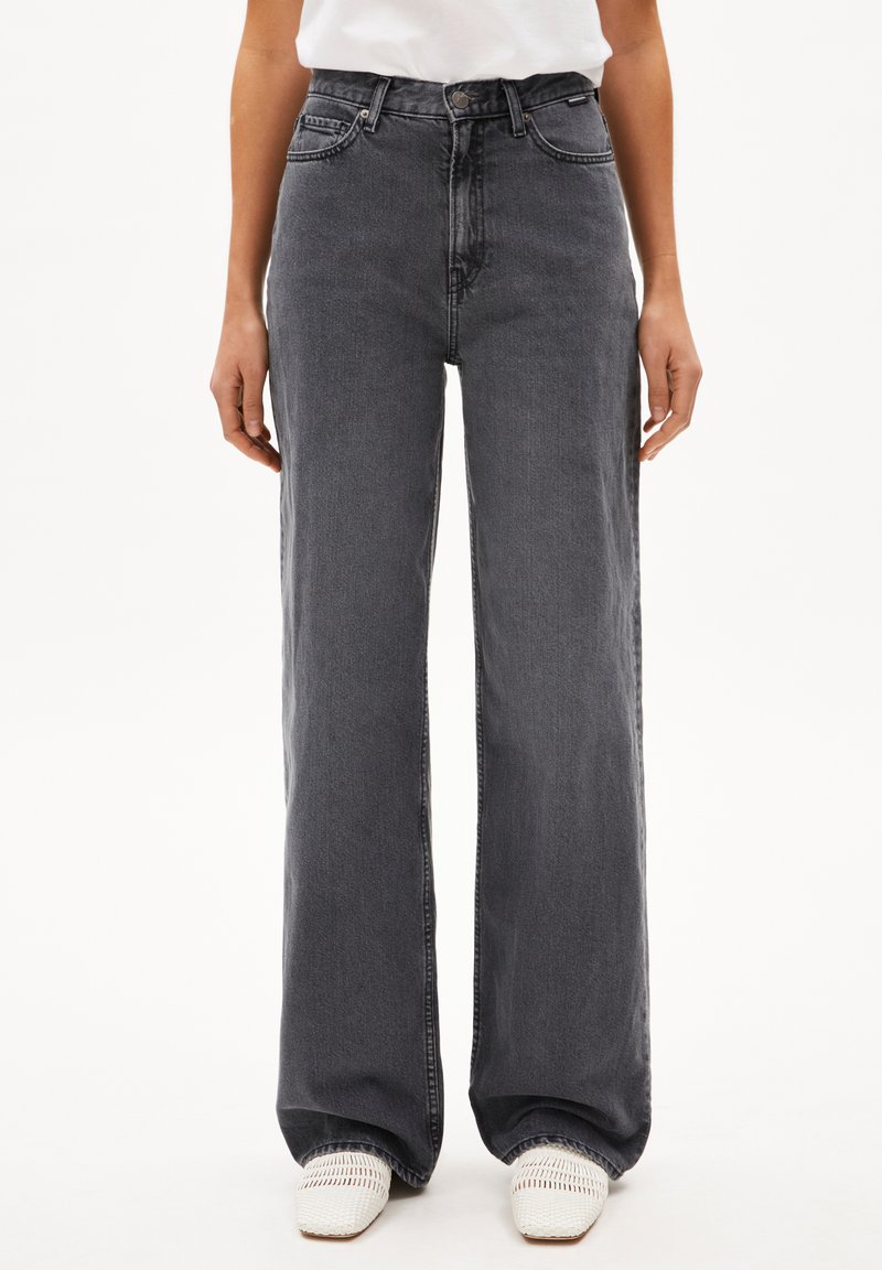Breda grå denimjeans med hög midja, framfickor och subtila blekningar. I kombination med vita vävda skor, inga ytterligare detaljer synliga.