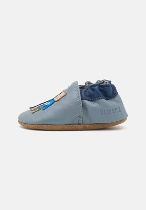 Chausson en cuir bleu doux avec une cheville navy froncée et une semelle en suède tan, arborant des détails brodés en bleu clair et foncé.