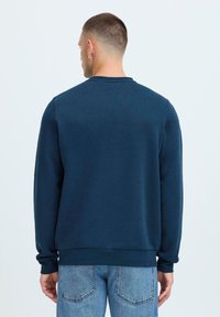 Sudadera de color azul marino con mangas largas, cuello redondo y puños de canalé. Tejido de algodón con una textura suave, diseño liso y sin patrones visibles.