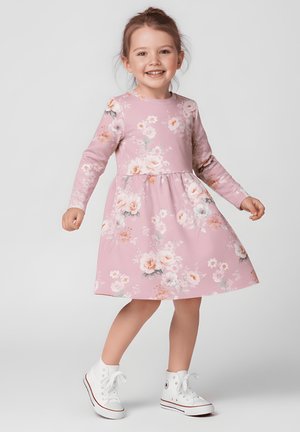 Różowa sukienka w kwiaty z długimi rękawami, okrągłym dekoltem i marszczoną talią. Do niej białe wysokie trampki.