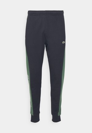 Schwarze Sweatpants mit grünen Seiteneinsätzen, elastischem Bund, engen Bündchen und weißem Druckdetail auf der linken Seite. Lacoste-Logo vorhanden.