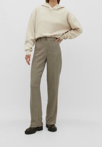Felpa beige chiaro con cappuccio e spalle basse abbinata a pantaloni a vita alta con motivo houndstooth marrone e crema e stivali con tacco alto neri.