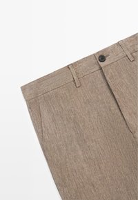 Pantaloni in lino beige con passanti per cintura, tasche laterali e chiusura con bottone nero in vita su sfondo bianco.
