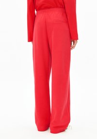 Rote Hosen mit weitem Bein aus weichem Stoff, ausgestattet mit einem elastischen Bund und einer kleinen Gesäßtasche. Glatte Textur und entspannte Passform.