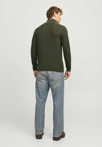 Dunkelgrüner Strickpullover mit strukturiertem Muster, gerippten Bündchen und Saum, kombiniert mit hellblauen Jeans und braunen Schuhen.