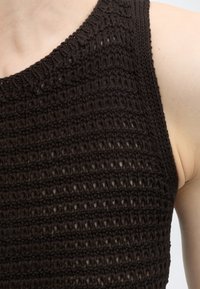 Gros plan d'une personne portant un haut noir sans manches en maille avec un motif texturé à maille ouverte.