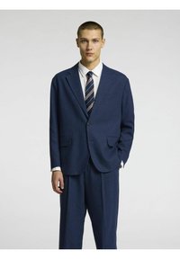 Costume bleu marine avec un revers cranté, un bouton unique et deux poches avant. Assorti à une chemise blanche et une cravate rayée. Conception sur mesure.