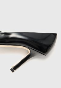 Musta lakattu nahka stiletto-korkokenkä, jossa on tyylikkäästi viistetty kärki ja teksturoitu vuori. Kannan juuressa on neliön muotoinen kultainen korostus.