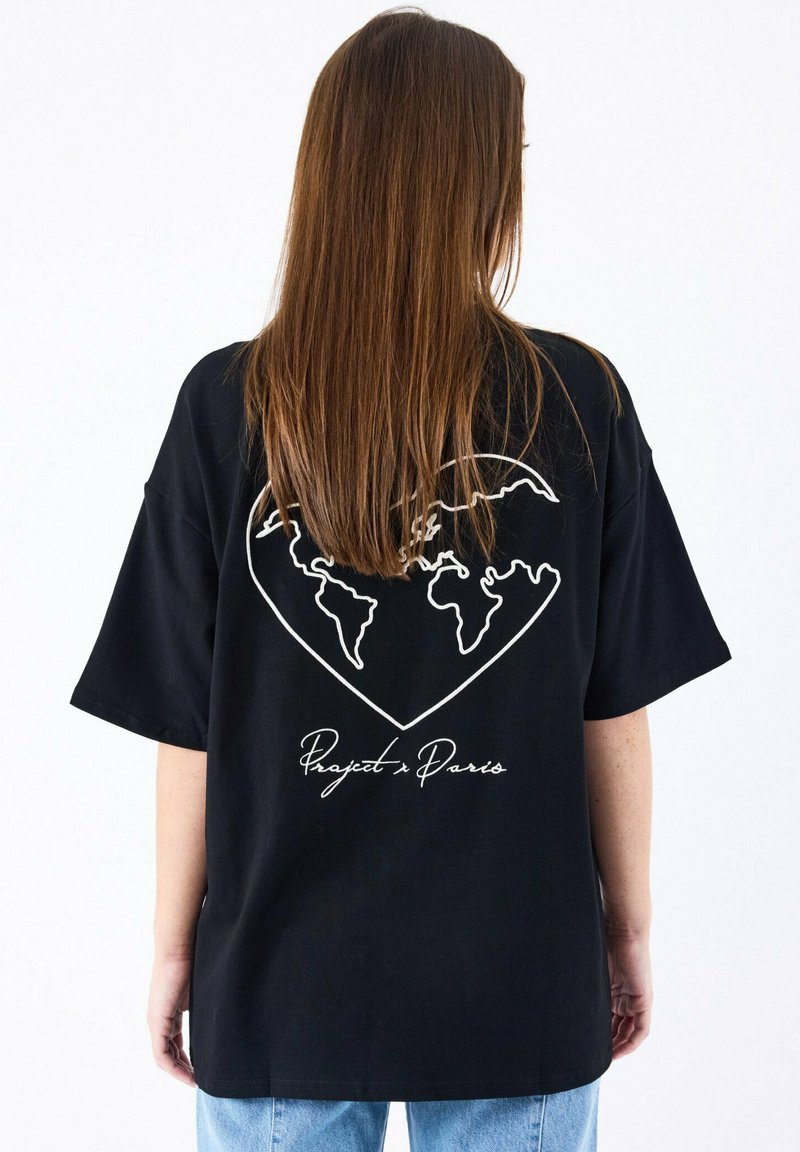 Camiseta negra de gran tamaño con un contorno blanco de un corazón que incluye un mapa del mundo y el texto "Proyecto París" debajo. Manga corta.