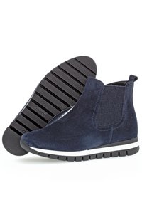 Bottines en suede bleu marine avec des côtés en élastique, bout rond et une bande blanche le long de la semelle en caoutchouc noire avec un motif texturé.