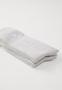 Chaussettes en coton grises, pliées, présentant un tissage texturé et un petit logo. Tissu doux et léger avec un design simple.