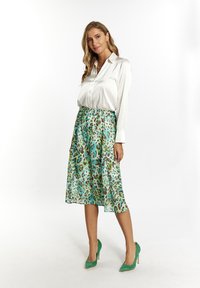 Blusa di raso bianco abbinata a una gonna leopardata verde teal. La gonna è lunga fino al ginocchio e svolazzante, caratterizzata da una texture morbida e una vita elastica.