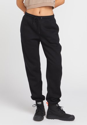 Black sweatpants with a drawstring waist, tapered leg design, and soft texture. Paired with black lace-up boots with an orange accent.
