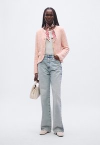 Világos rózsaszín texturált dzseki, fehér felső, magas derekú világoskék farmer, krémszínű kézitáska és bézs cipő, virágos sál kiegészítővel.