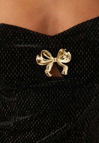 Svart texturerad tyg med en glänsande guldslöja i form av en båge i centrum. Designen har en subtil lyster med intrikata mönster.