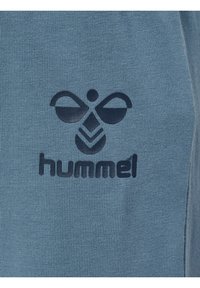 Ljusblå bomullströja med en mörk logotyp bestående av abstrakta former och texten "hummel" i mitten, mot en ribbad textur.