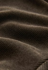 Dunkelbrauter Stoff mit einer weichen Textur, der subtile Rippmuster aufweist. Das Material erscheint dick und leicht in Falten organisiert.