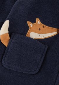 Navy-Fleece-Bekleidung mit einer Tasche, die ein Fuchs-Gesicht-Design in Beige, Weiß und Braun zeigt, und ein weiches Material sowie verspielte Details aufweist.