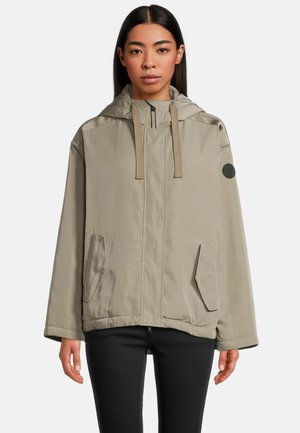 Lichtbeige hoodie gemaakt van soepel materiaal. Bevat een ritssluiting, twee voorzakken en een ronde logo patch op de mouw.