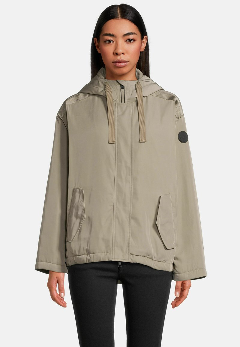 Helle beige Kapuzenjacke aus glattem Material. Mit Reißverschluss, zwei Fronttaschen und einem runden Logo-Patch am Ärmel.