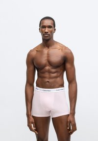 Ροζ βαμβακερά μπόξερ με μαύρη ζώνη Calvin Klein στη μέση, εφαρμοστό σχέδιο και λεία υφή, φορεμένα από ανδρική φιγούρα.