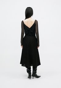 Sort kjole med silky top med draperet ryg og en tekstureret nederdel med mønstret finish. Kombineret med knæhøje sorte støvler.