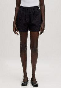 Zwarte, gestructureerde shorts met een elastische tailleband, voorzien van zijzakken en een ontspannen pasvorm. Draagt met een eenvoudige witte tanktop en flats.