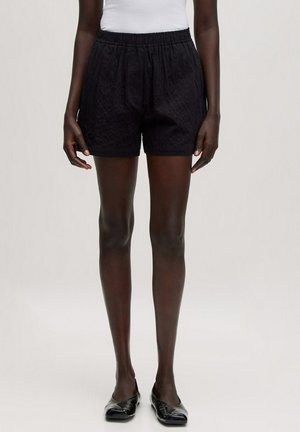 Shorts noirs texturés avec une taille élastique, dotés de poches latérales et d'une coupe décontractée. Portés avec un débardeur blanc uni et des ballerines.