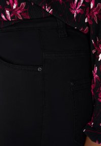 Jean en denim noir avec une poche avant dotée d'un bouton en métal. Le tissu a une texture lisse, associé à un haut à motif floral.