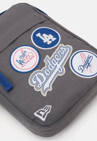 Sacchetto di tessuto grigio con loghi dei Dodgers ricamati in blu e bianco e toppe rotonde, tra cui "All-Star Game" e un design di baseball.
