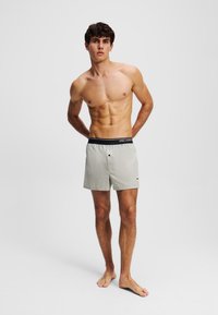Helle graue Badehose mit einem schwarzen elastischen Bund, der ein kleines Logo trägt. Das Design ist schlicht und gerade geschnitten und besteht aus leichtem Material.