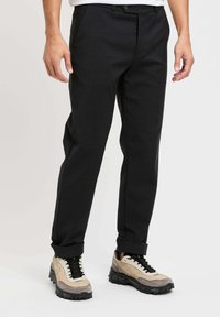 Pantaloni neri, taglio sartoriale con una texture liscia e linea dritta. Presentano tasche anteriori, chiusura con bottone e orli arrotolati.