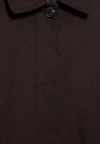 Brun uldblandet frakke med en tekstureret finish, der har en knaplukning og klassisk krave. Synlig syning langs frontpanelet.