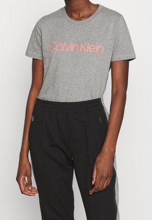 Osoba nosząca szary t-shirt Calvin Klein oraz czarne spodnie z elastycznym pasem i bocznymi kieszeniami na zamek.