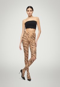 Collant trasparenti a strisce tigre in colore nudo, caratterizzati da audaci strisce nere. Abbinati a tacchi a spillo neri e a un crop top nero.