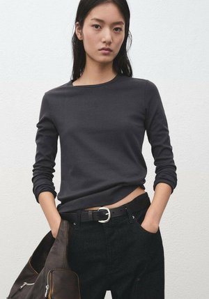 Long-sleeve, dark gray top in a soft material, round neckline, paired with high-waisted black jeans and a brown shoulder bag.