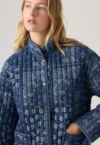 Gequilte denim jas in donkerblauw met witte paisley patronen, voorzien van een hoge kraag en drukknoopsluiting, textuurstof en zijzakken.