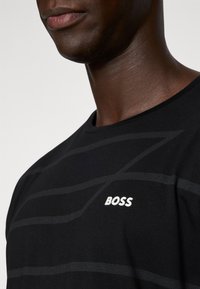 Melna kokvilnas t-krekls ar apaļu kaklu. Iezīmēts ar smalkām horizontālām svītrām un baltu "BOSS" logo kreisajā krūšu daļā.