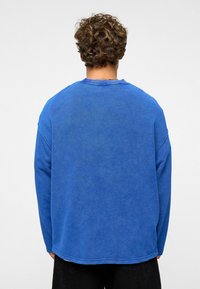 Blauwe sweatshirt met lange mouwen, relaxed fit, geribbelde halslijn en een zachte textuur, met verlaagde schouders en een afgeronde zoom.