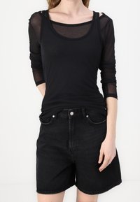 Černý dlouhý rukáv top s průhlednou texturou navrstvený přes černý tílko, spárovaný s černými džínovými šortkami s vysokým pasem.