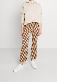 Beige hoodie med ficka fram, matchad med bruna och beige rutiga vida byxor och vita sneakers.