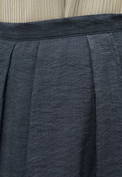 Κοντινή λήψη φούστας από σκούρο γκρι υφασμάτινο ύφασμα με ρυτίδες και πτυχώσεις στη μέση, συνδυασμένη με μπεζ μπλουζάκι από ριμπ ύφασμα.