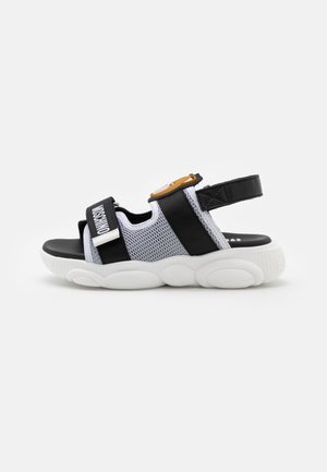 Sandálias em preto e branco com parte superior em rede, tiras ajustáveis e sola texturizada. Detalhe de hardware notável em laranja na tira. Design casual.