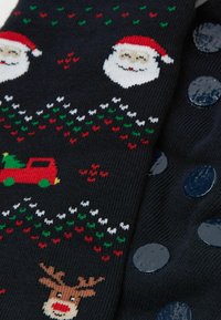 Ciemnoniebieski sweter z festiwalowymi wzorami: twarze Świętego Mikołaja, renifery i czerwony samochód. Wzory w kolorze czerwonym, zielonym i białym; teksturowany, miękki materiał z okrągłymi niebieskimi guzikami.