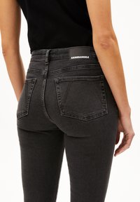 Jean noir taille haute au design ajusté, fabriqué en denim. Présente deux poches arrière et une étiquette de marque Armendangels sur la taille.