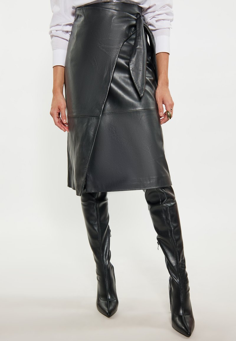 Zwarte leren wikkelrok met een zijstrikdetail, gladde textuur, middellange snit, gecombineerd met zwarte kniehoge puntige laarzen.