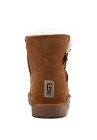 Botín de ante marrón con un suave forro blanco, punta redonda y un botón lateral decorativo. Presenta una suela de goma texturizada y un parche con logotipo.