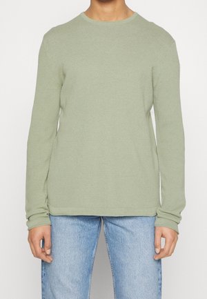 Pulls à col rond à manches longues en vert clair, fabriqué à partir d'un tissu tricoté texturé. Il présente une coupe décontractée et des poignets côtelés, associé à un jean bleu.