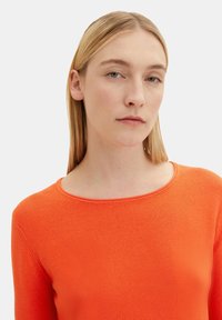 Leuchtend orangefarbener Pullover mit strukturiertem Strick, Rundhals-Ausschnitt und langen Ärmeln. Glatte Stoffoberfläche und taillierte Silhouette.